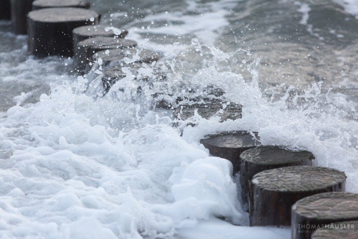 deutschland - Welle durchbricht eine Buhnenreihe. Eine kleine Welle trifft auf eine Buhne und das Wasser spritzt empor.