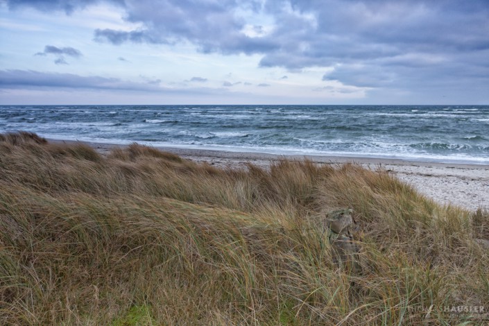 deutschland - Blick über die Grasduene auf eine bewegte Ostsee mit Wellengang und einem stark bewoelkten Himmel.