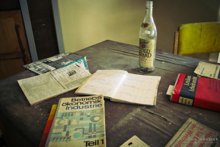 Lost Places - Schreibtisch mit alten Büchern und Heften und einer leeren Flasche Goldbrand