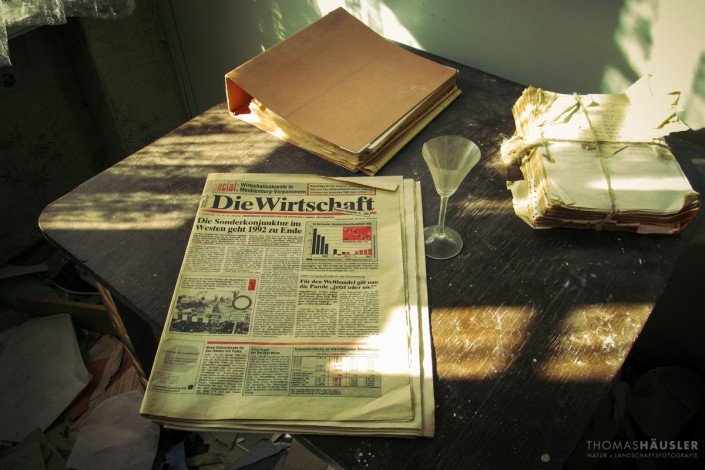 Lost Places - Ein Tisch mit einer alten Zeitung aus dem Jahre 1992 und einigen anderen Unterlagen und einem leeren Schnapsglas.